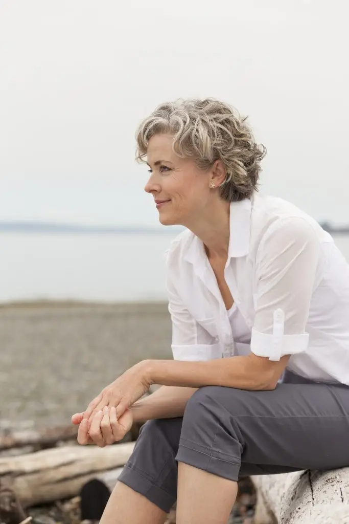 Beautiful, happy, healthy, smiling, middle aged mature woman sitting outdoors on beach