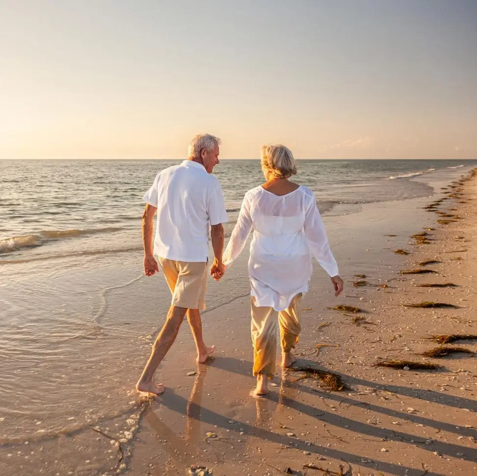 Happy senior man and woman old retired couple walking and holding hands on a beach at sunset