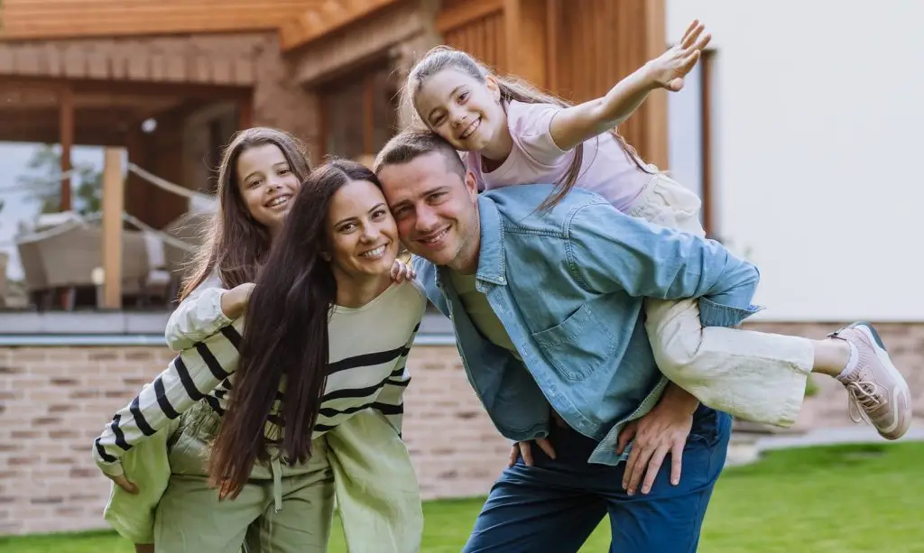 Beautfiul young family standing in front their family home enjoying together time, laughing, having fun.