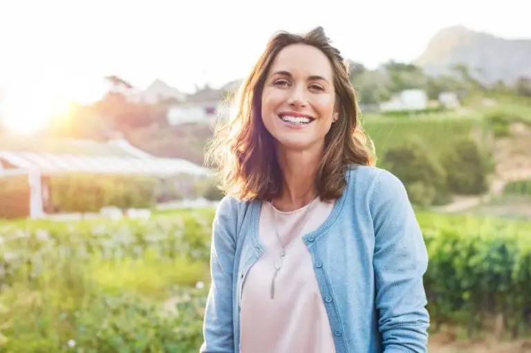 Cheerful mature woman enjoying in park during sunset. Happy hispanic woman in casual feeling relaxed outdoor. Smiling brunette woman looking at camera with carefree.